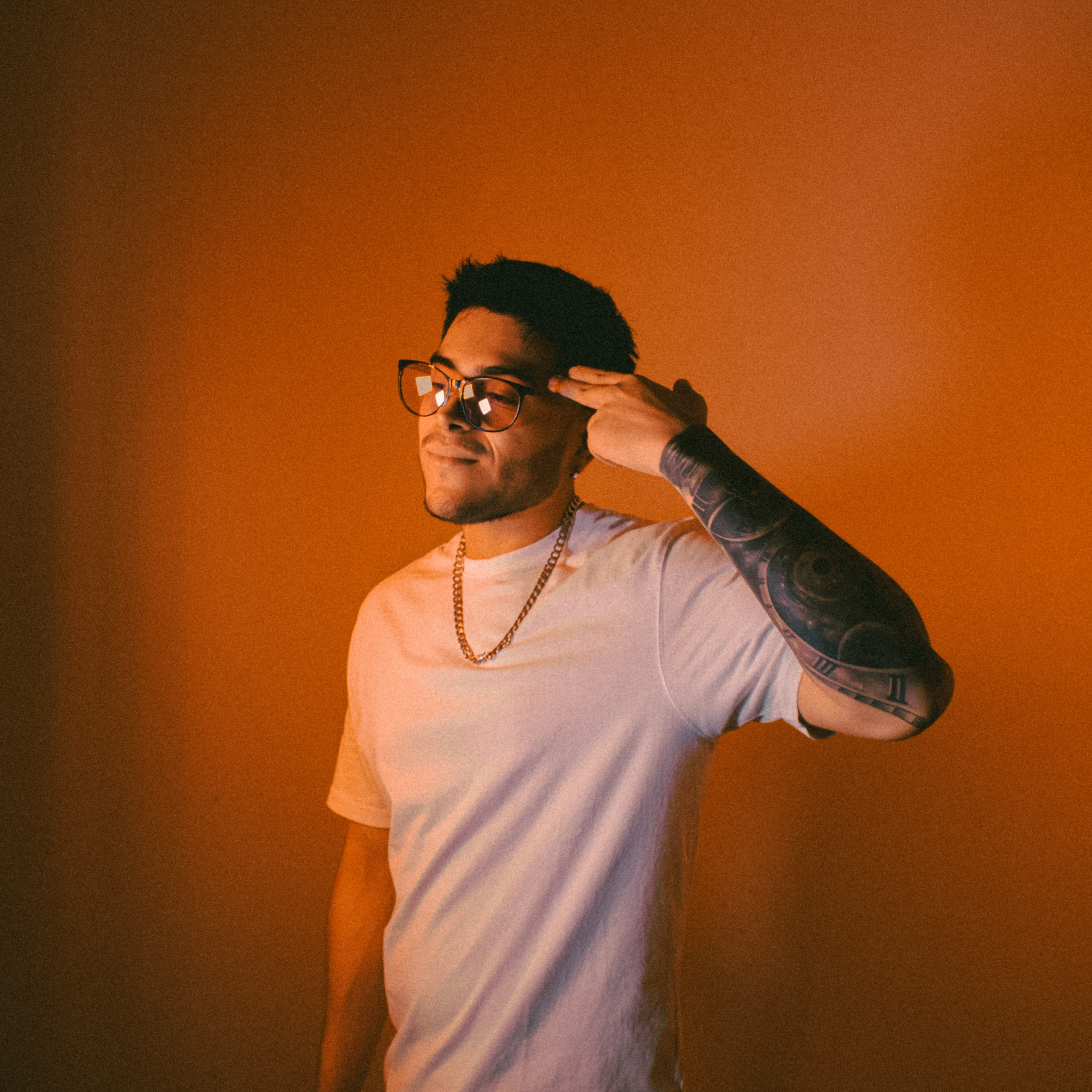 Color naranja, persona con tatuajes haciendo su seña de artista